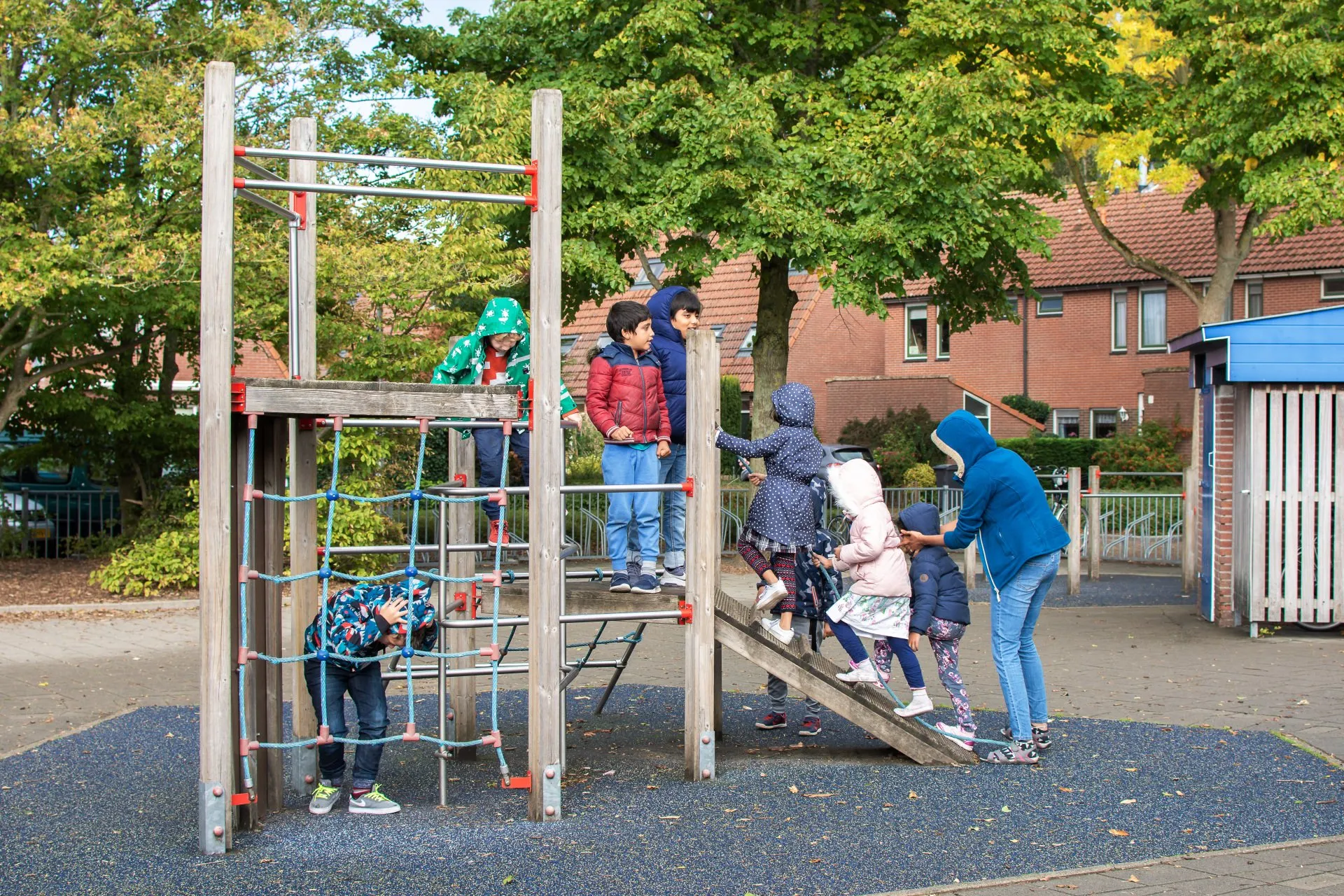 Children playing on an outdoor climbing frame with a teacher nearby
