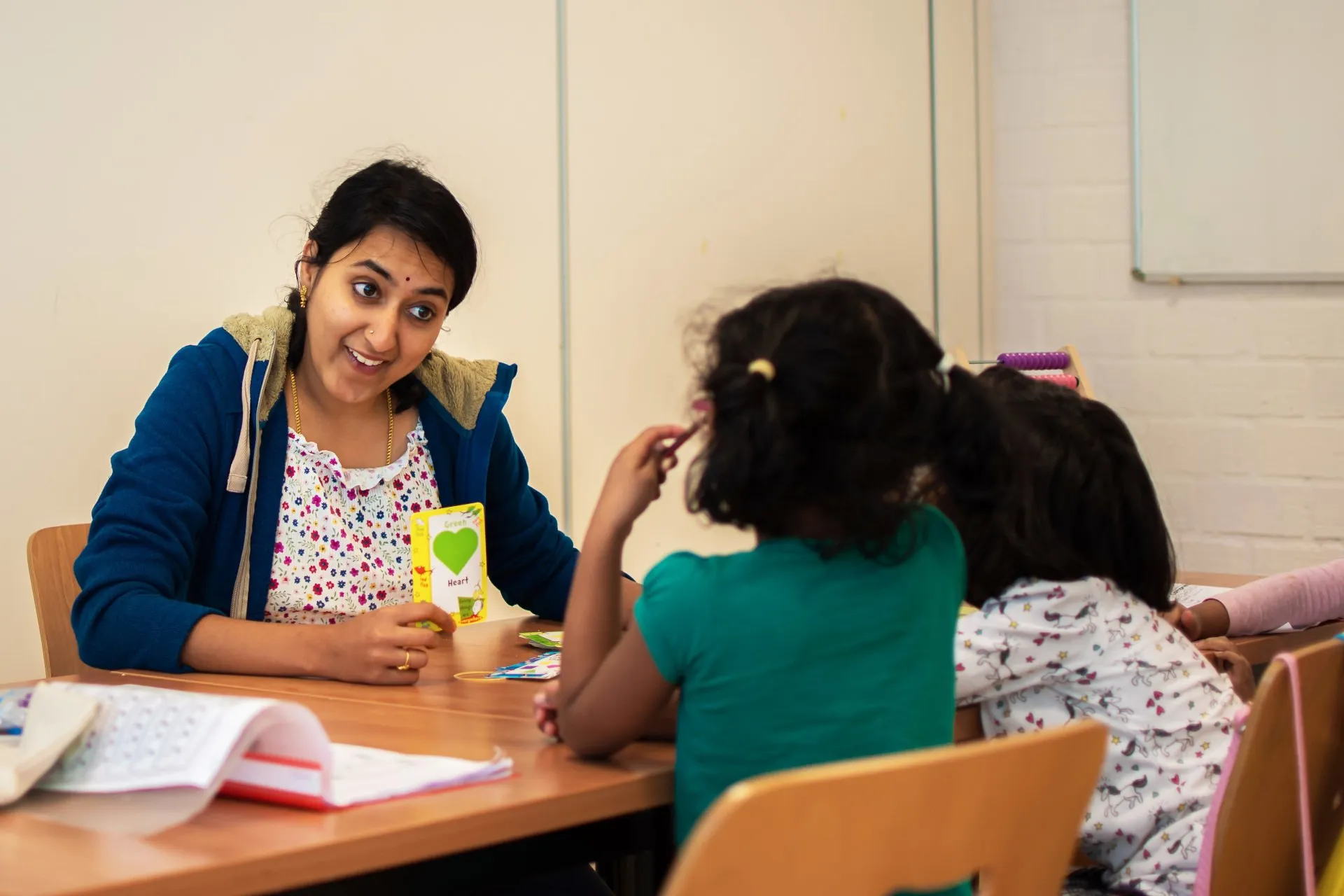 A teacher using picture flashcards with two young girls at a table