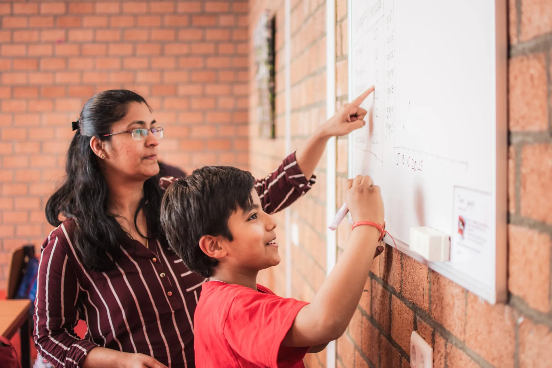 A boy working through a maths problem on the whiteboard with his teacher