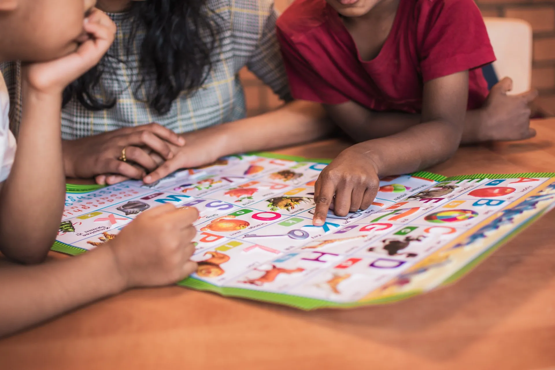 A teacher and two children reading a colourful alphabet chart together