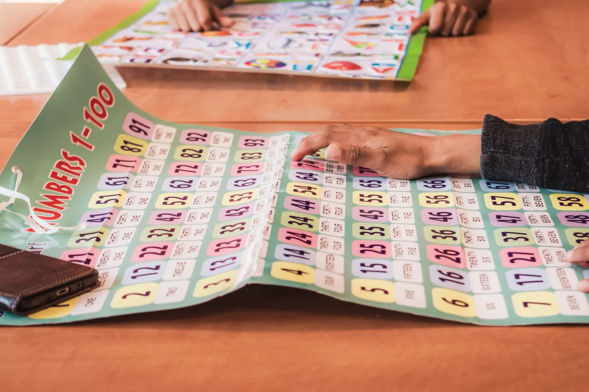 A child exploring a 'Numbers 1 to 100' learning chart with a teacher